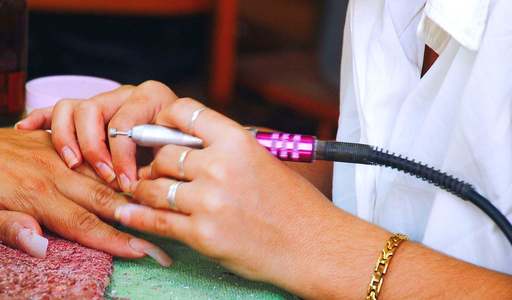 Close-up image of a nail technician using an electric file on a client's nails during a manicure session.